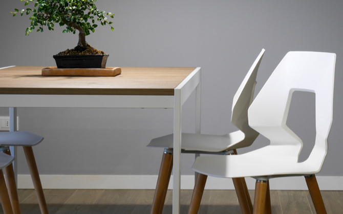 small wooden table with plant on top. Two cool white chairs, one tucked in, one tucked out.